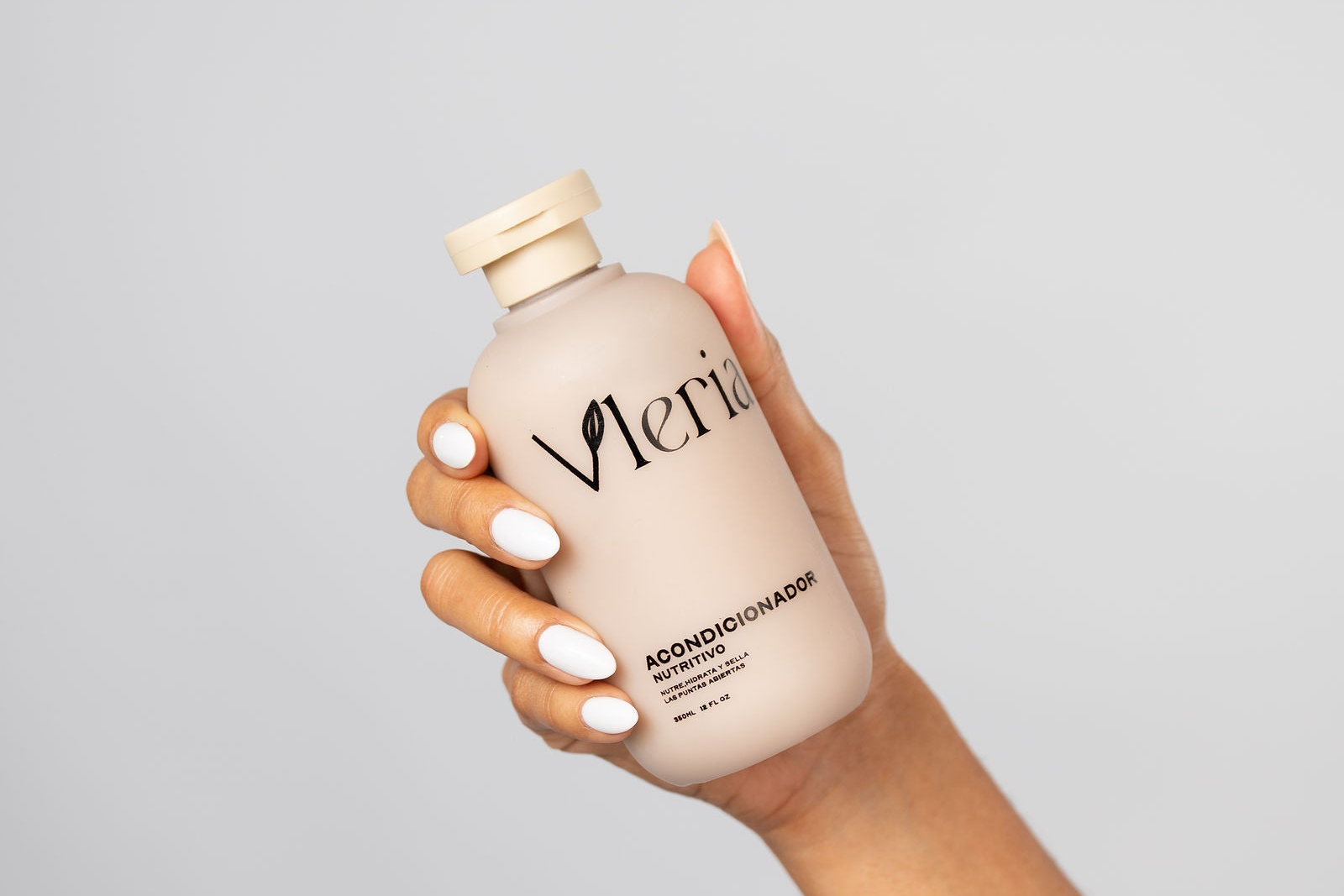 Hand holding a bottle of Vleria conditioner against a gray background